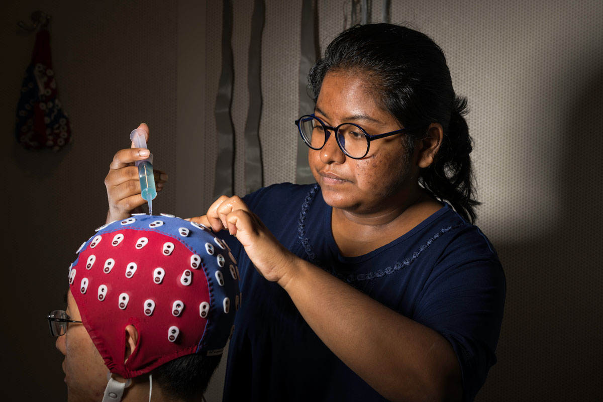 Senior biomedical engineering student Sophea Urbi Biswas adjusts an electroencephalography cap on fellow lab member Jin Dou, a biomedical engineering PhD student.